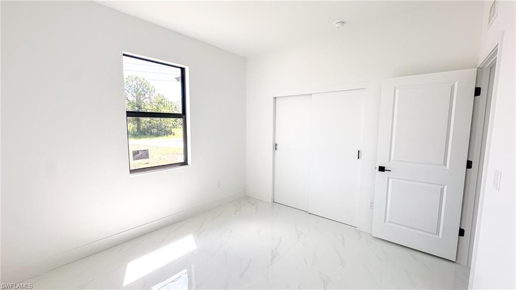 Bright interior with white walls, a single pane window, white panel door with black hardware, and an adjacent white sliding closet door, all complemented by light-toned tile flooring