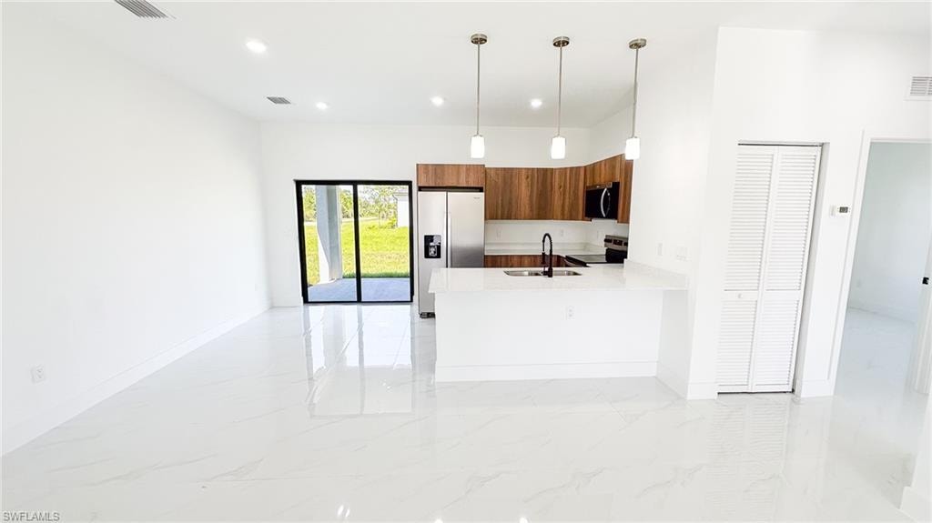 Open-concept kitchen and living area featuring polished concrete flooring, white quartz countertops, wood-finish cabinetry with pendant lighting, stainless steel appliances, and abundant natural light from glass sliding doors