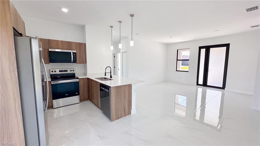 Open-concept kitchen and living area featuring wood-finish cabinetry, stainless steel appliances, a white stone countertop island, and large format white tile flooring