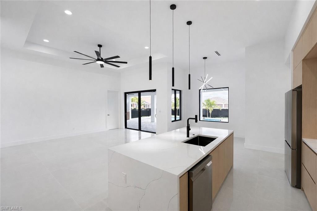 Kitchen with modern cabinets, a kitchen island with sink, stainless steel appliances, light stone countertops, and suspended lighting
