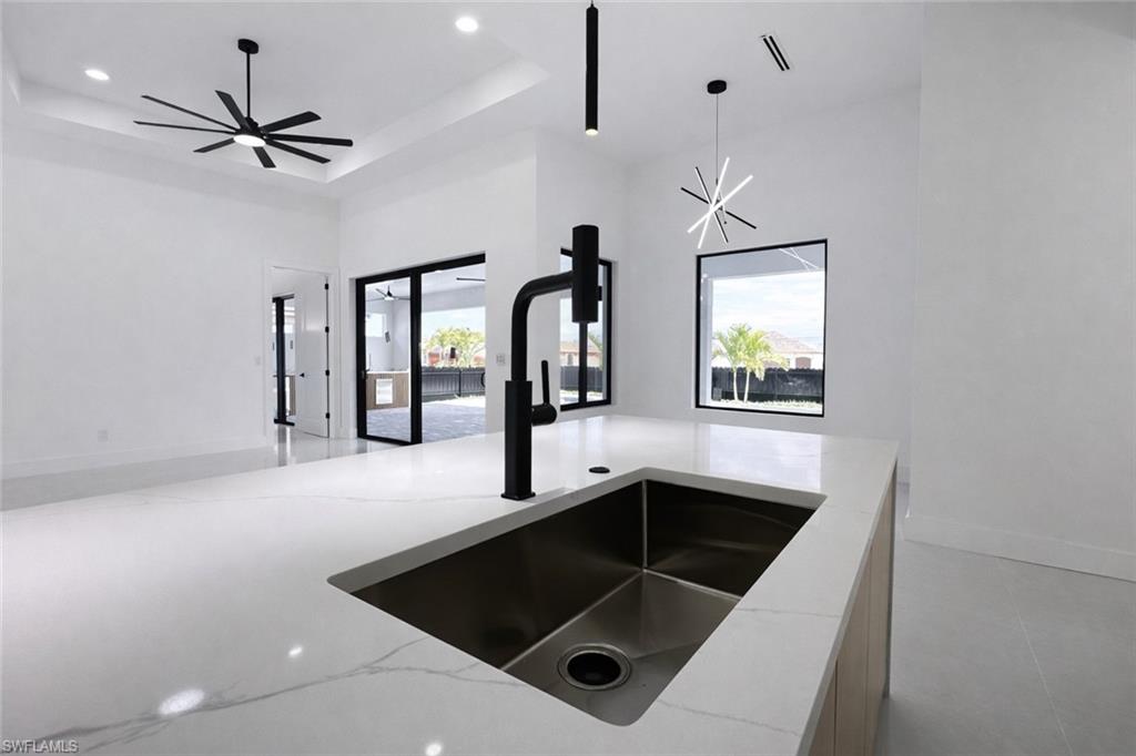 Kitchen featuring light stone counters, a tray ceiling, open floor plan, and hanging light fixtures