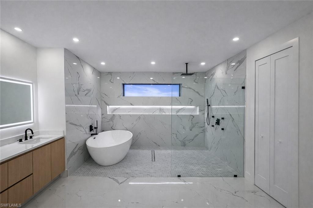 Full bath with a marble finish shower, stone wall, recessed lighting, vanity, and a freestanding tub