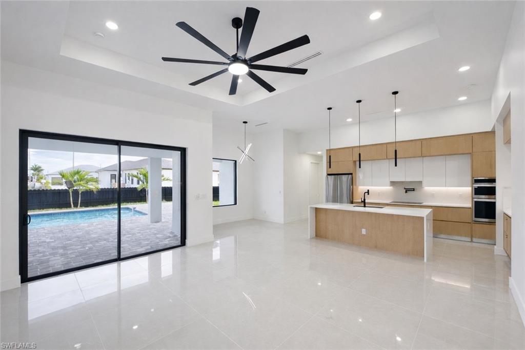 Dual tone kitchen featuring open floor plan, a large island with sink, modern cabinets, decorative light fixtures, and a raised ceiling