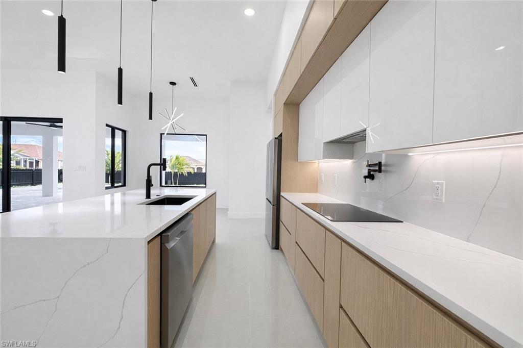 Kitchen with two tone cabinetry, modern cabinets, light stone counters, a large island, and stainless steel appliances
