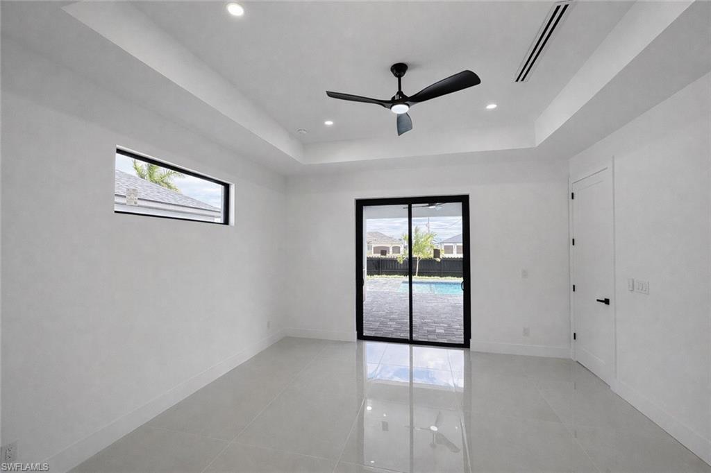 Spare room with healthy amount of natural light, ceiling fan, a tray ceiling, light tile patterned flooring, and recessed lighting