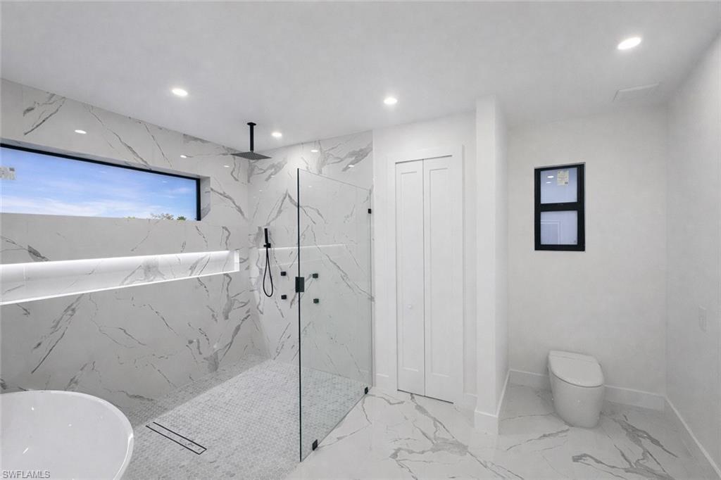 Bathroom with a marble finish shower, a soaking tub, recessed lighting, light marble finish floors, and a closet