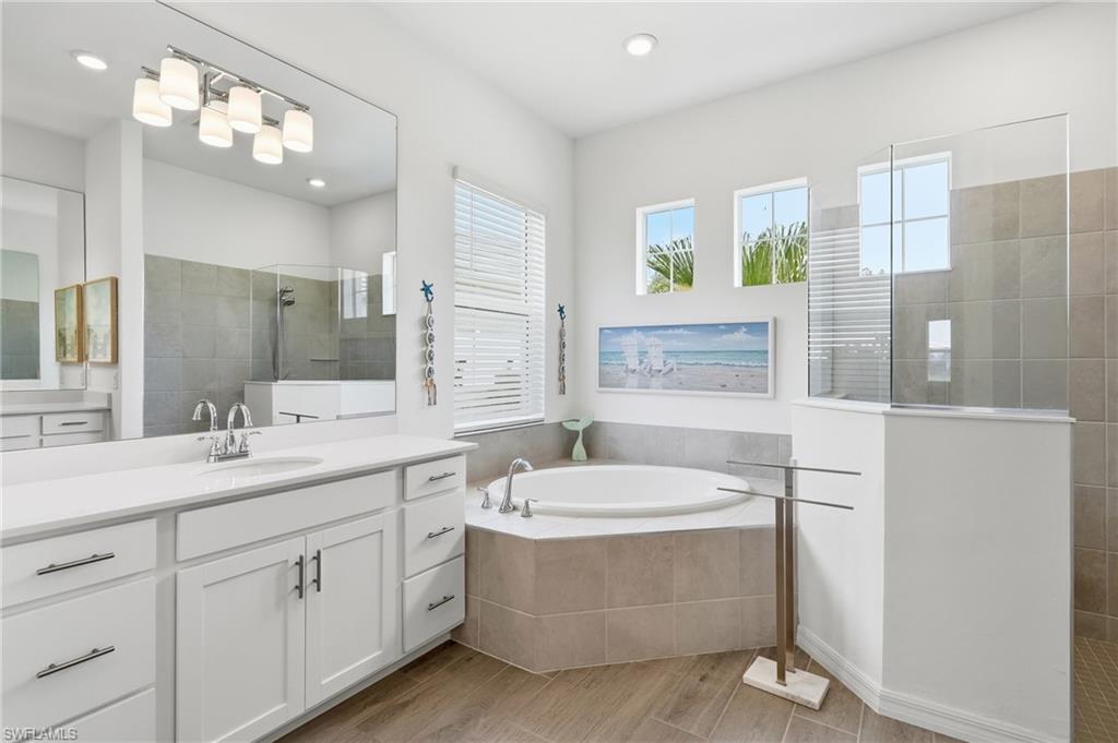 Dual vanity with white cabinetry, soaker tub, and walk in shower