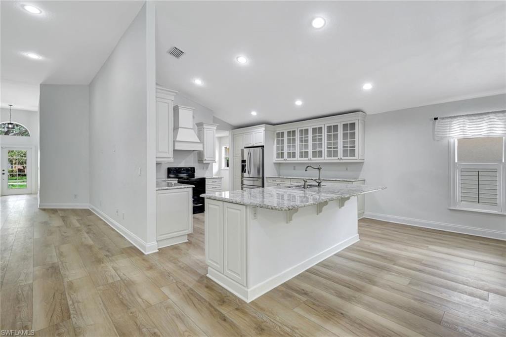 Spacious kitchen with a central island, white cabinetry, integrated range hood, and wood-finish flooring