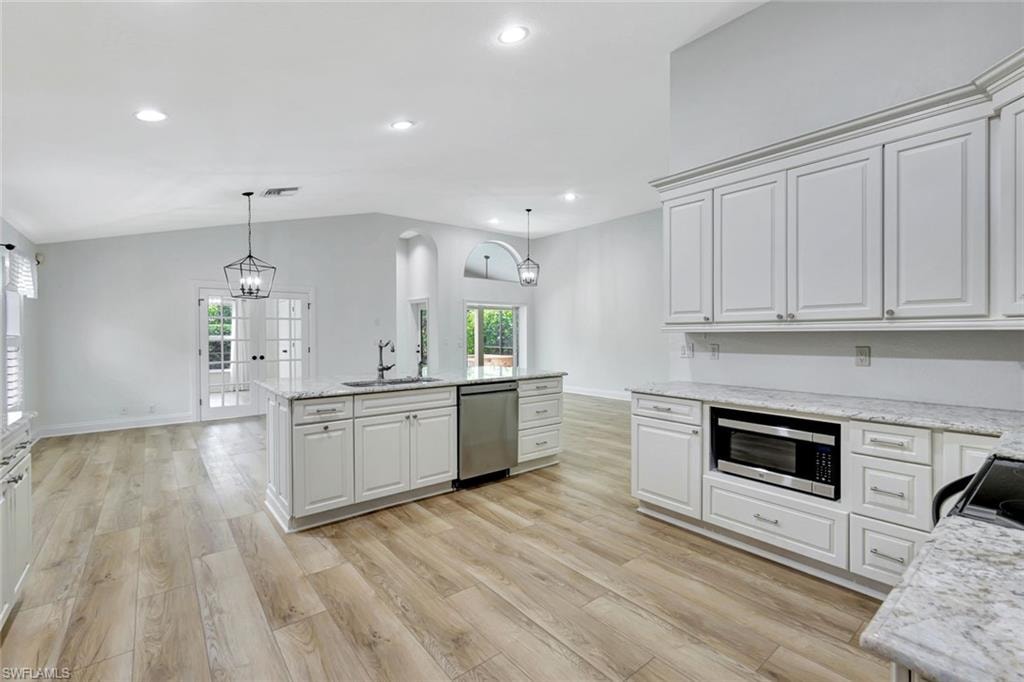 Open-concept living space with vaulted ceilings, wood-finish flooring, and white cabinetry