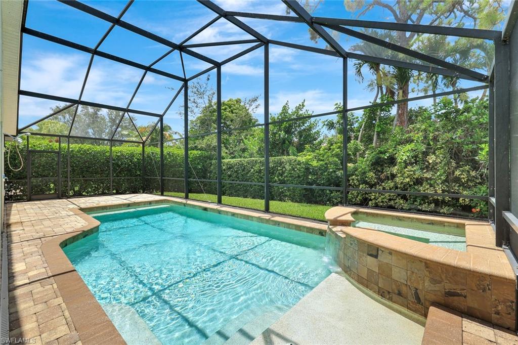 Screened outdoor pool with a natural stone-tiled spa and paver decking