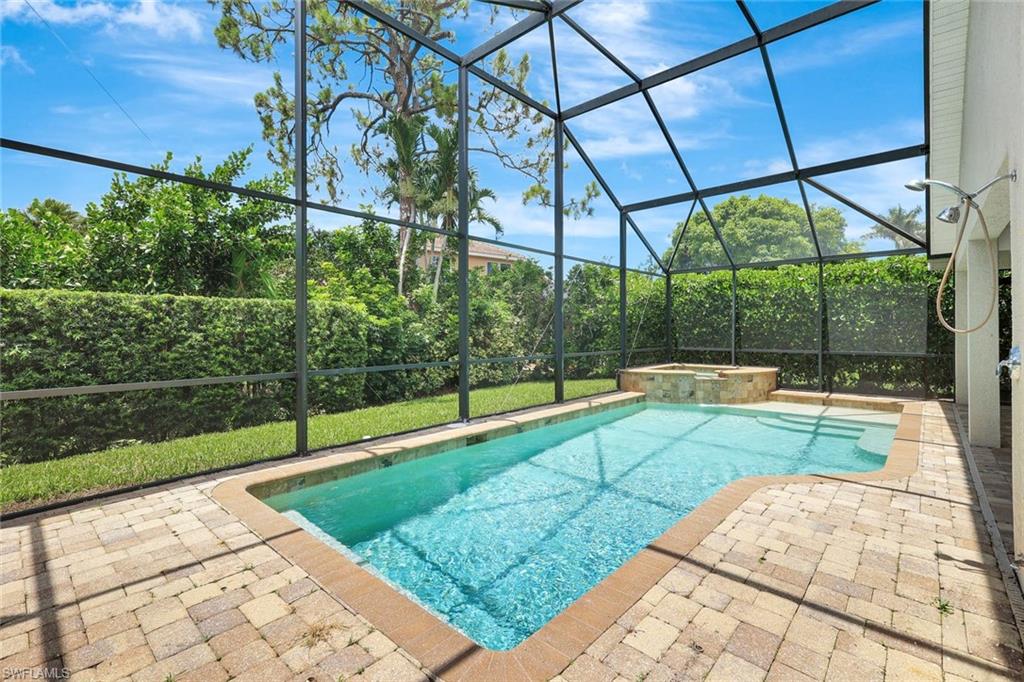Screened-in pool deck featuring a swimming pool, integrated spa, and paver surfacing