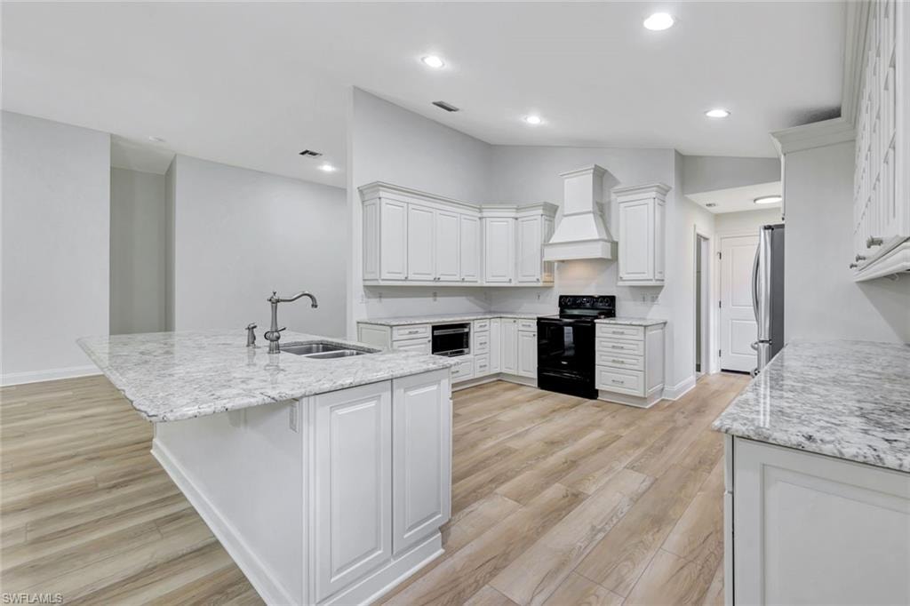 Kitchen featuring light wood-finish flooring, white cabinetry, a built-in oven, and a large central island with an integrated sink and light-toned countertop