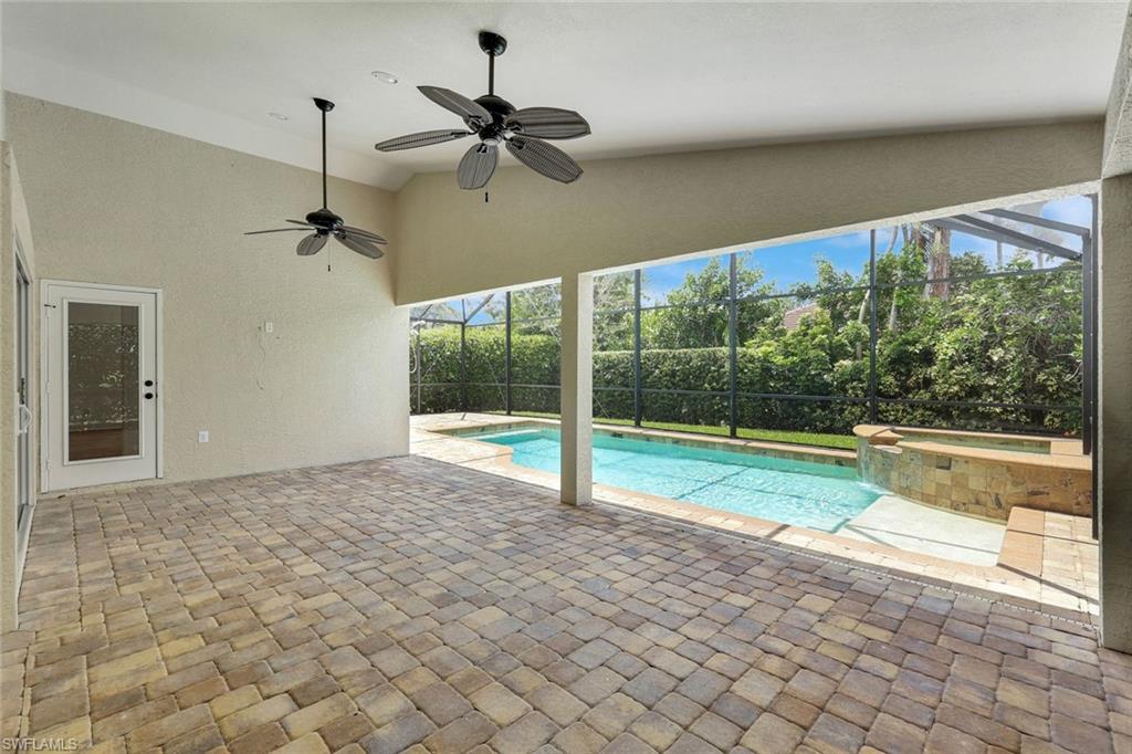 Screened lanai featuring paver flooring, dual ceiling fans, and a built-in spa with a water feature