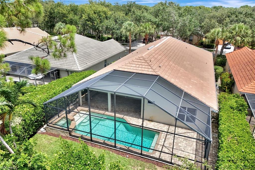 Screened-in pool with paver decking, integrated spa, and surrounding mature landscaping