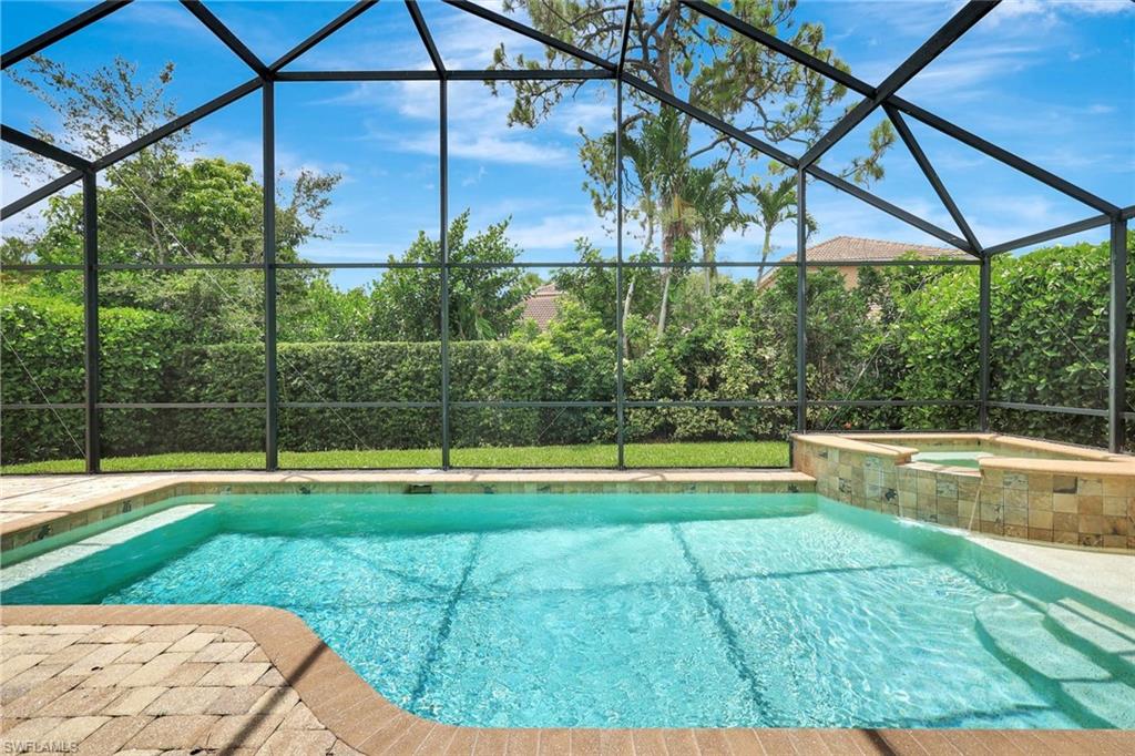 Screened-in outdoor pool featuring a hot tub with a stone-finish facade, integrated waterfall, and paved deck surround