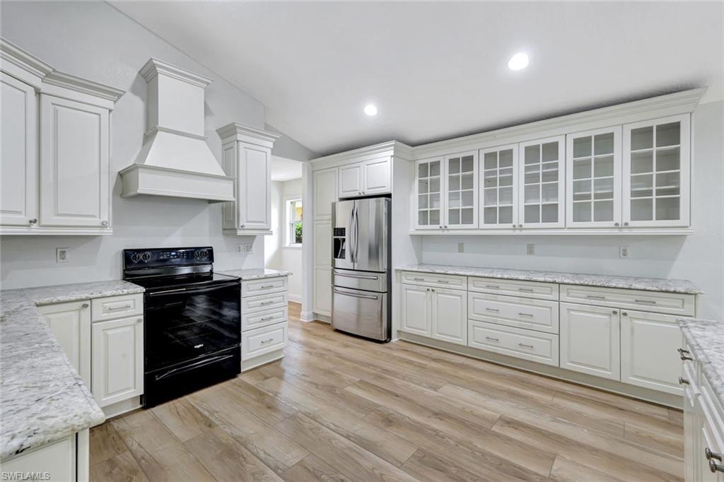Recessed lighting, wood-finish flooring, white cabinetry, stainless steel refrigerator, and light-toned countertops