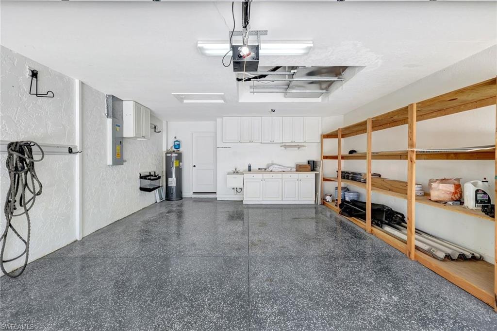 Epoxy-coated concrete flooring, built-in shelving, white cabinetry, utility sink, and overhead fluorescent lighting