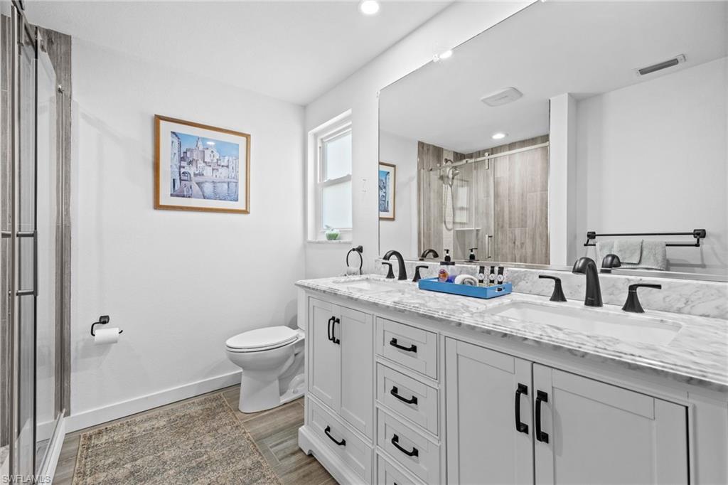 Dual sink vanity with stone countertop, white shaker cabinetry, and matte black fixtures