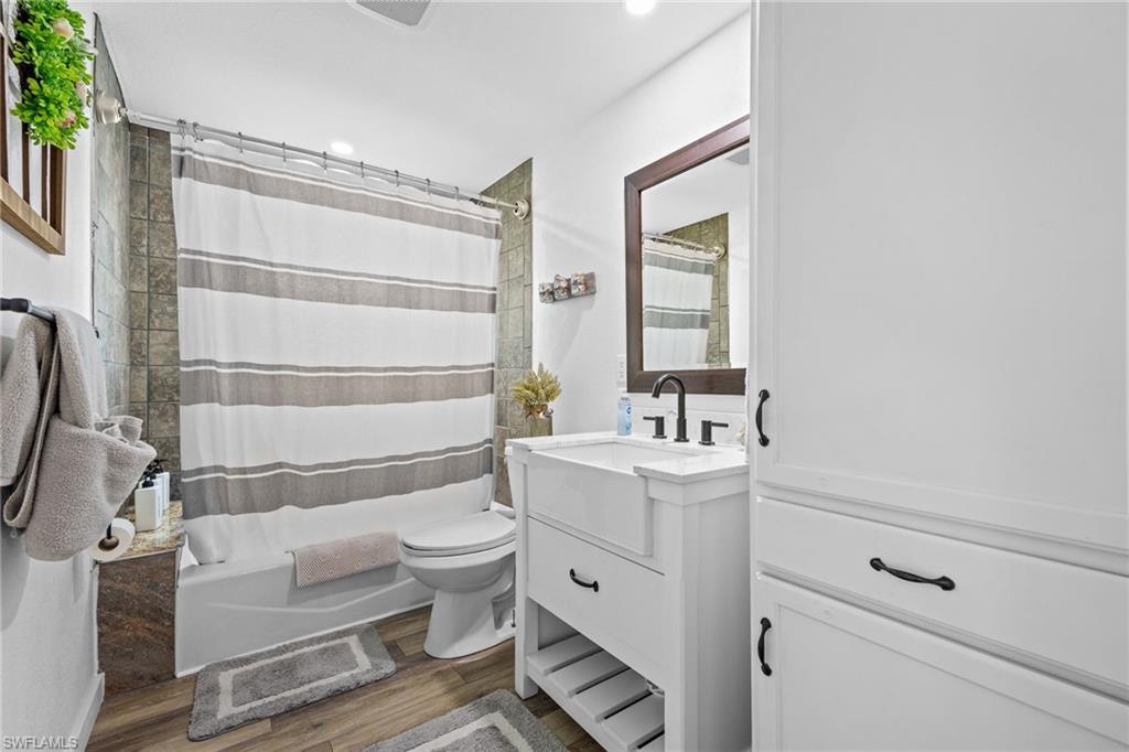 White shaker vanity with farmhouse sink, dark bronze fixtures, wood-finish flooring, built-in storage cabinetry, and subway tile shower surround