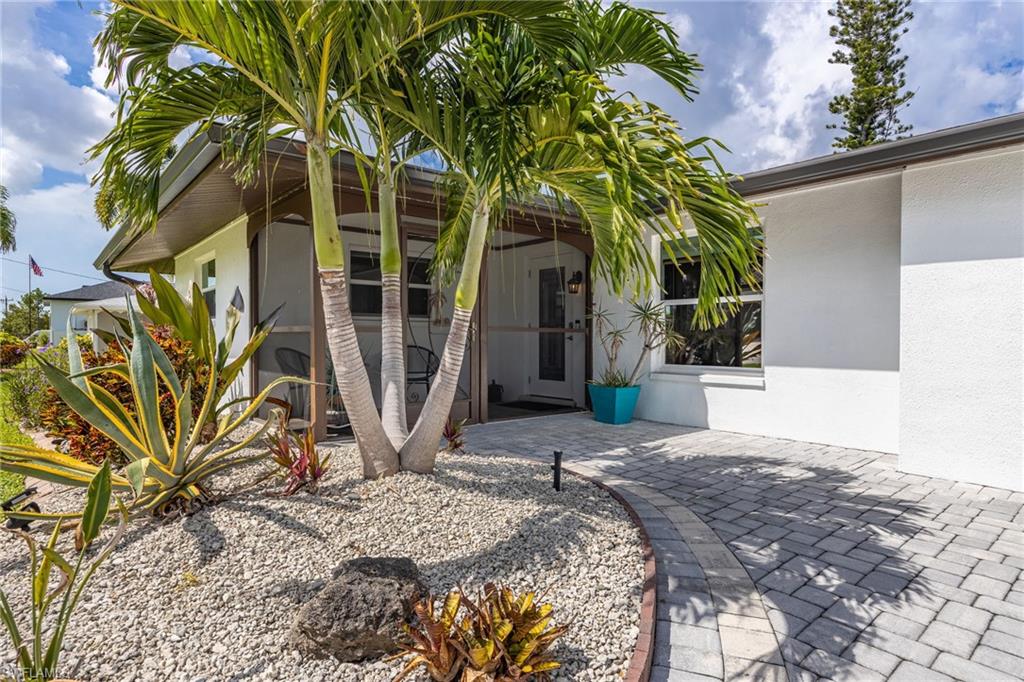 Paver pathway leading to a screened entryway, white stucco exterior, and low-maintenance landscaping with tropical plantings