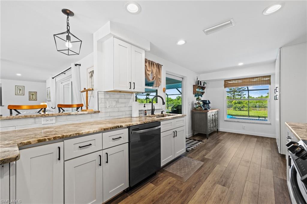 White cabinetry, wood-finish flooring, undermount sink with a matte black faucet, recessed lighting, and a window overlooking exterior landscaping