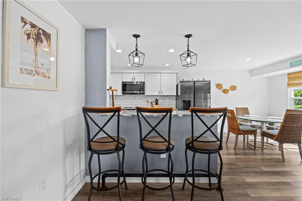 Breakfast bar with pendant lighting, wood-finish flooring, white cabinetry, and stainless steel appliances