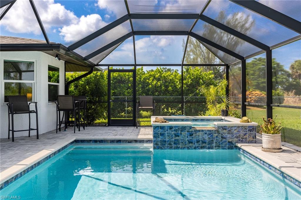 Screened pool enclosure with a geometric pool, integrated spa with blue tile surround, and a paver deck