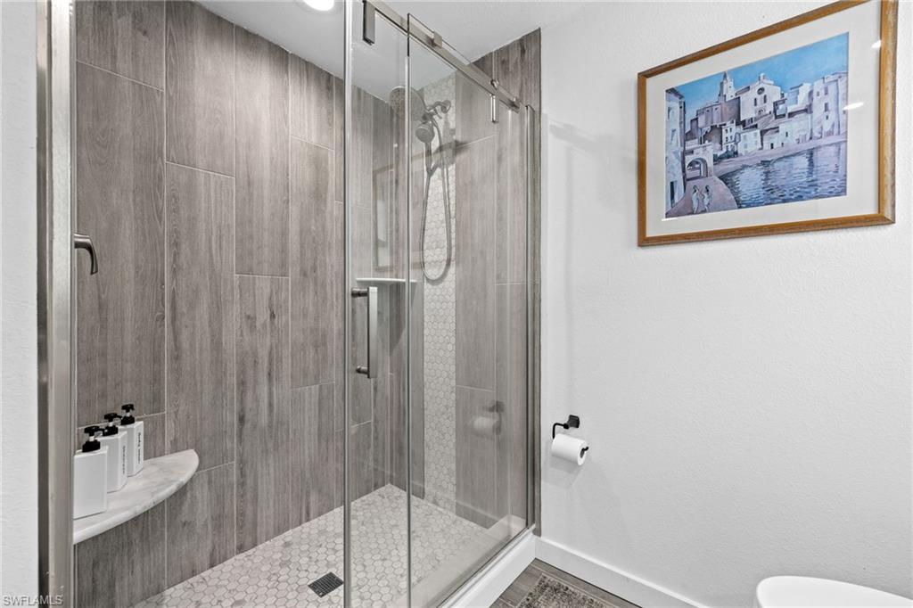 Glass-enclosed shower with a wood-look tiled wall and a hexagonal tile floor