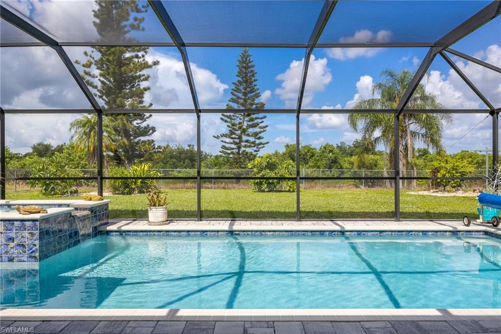 Screened enclosure featuring a swimming pool with a waterfall spa, paver deck, and extensive green space