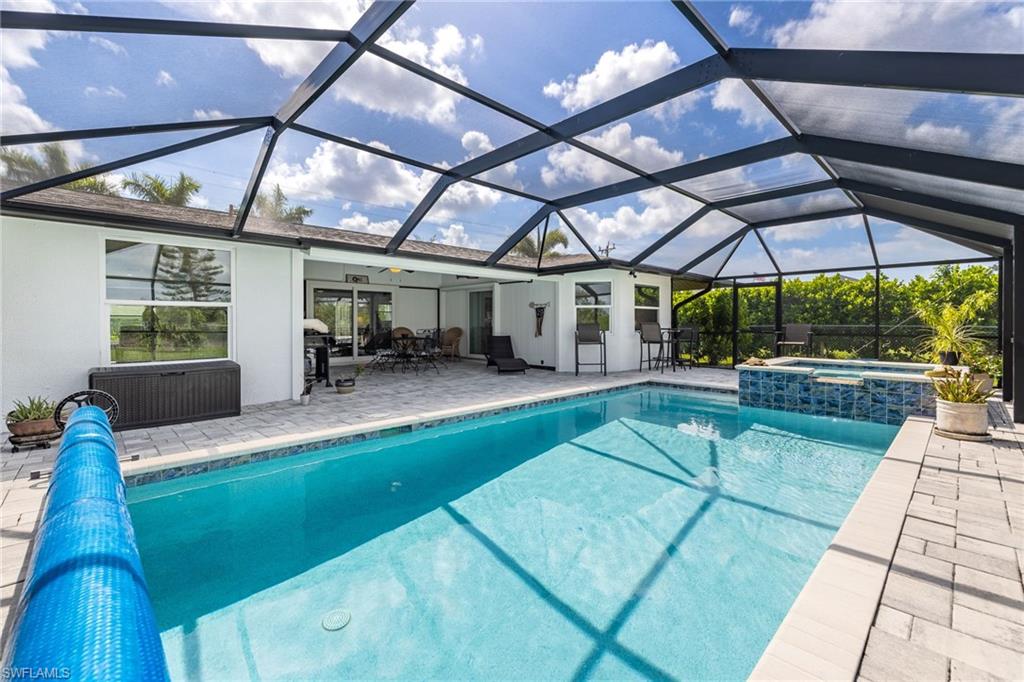 Screened-in outdoor living space with a swimming pool, integrated spa, and paver decking
