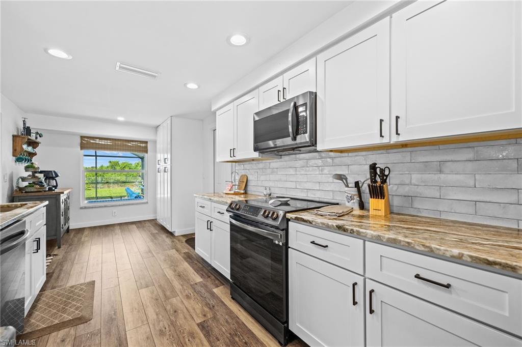 White shaker-style cabinetry, stainless steel microwave, stone countertops, subway tile backsplash, and wood-finish flooring