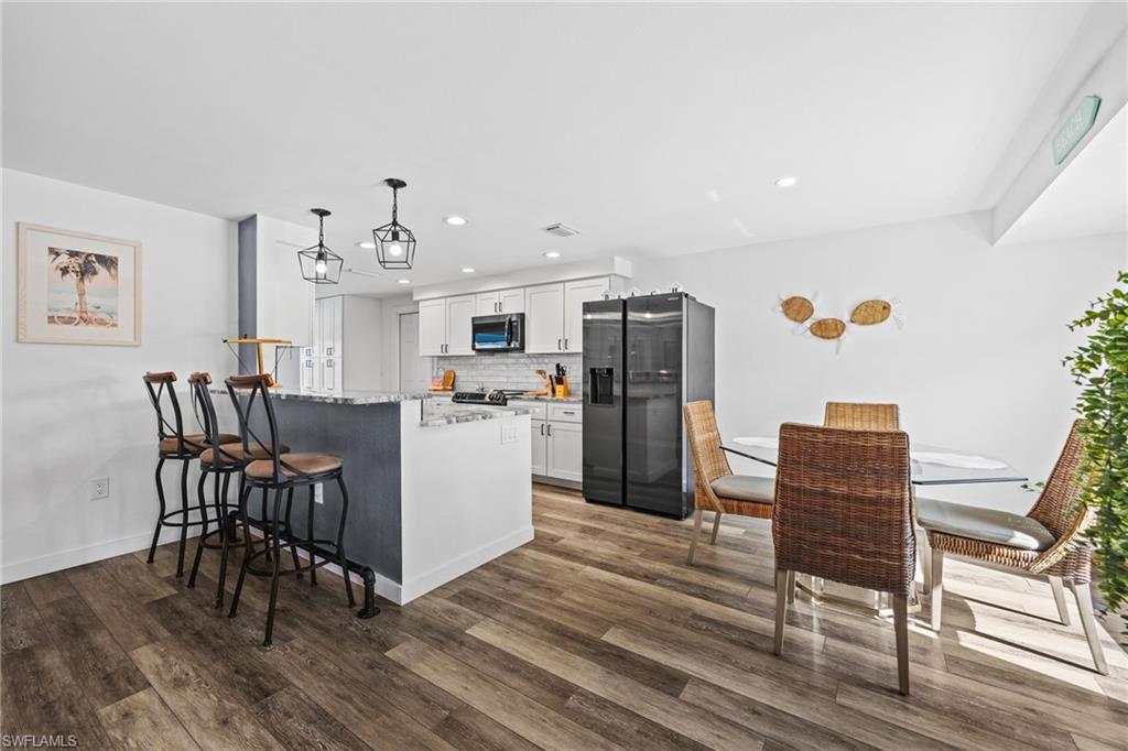 Open-concept kitchen featuring wood-finish flooring, white cabinetry, integrated appliances, and a breakfast bar with pendant lighting