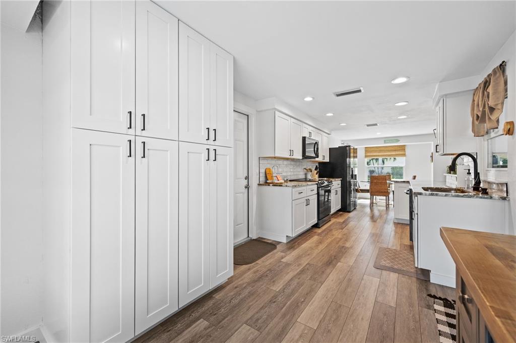 Crisp white cabinetry, wood-finish flooring, recessed lighting, and a white subway tile backsplash