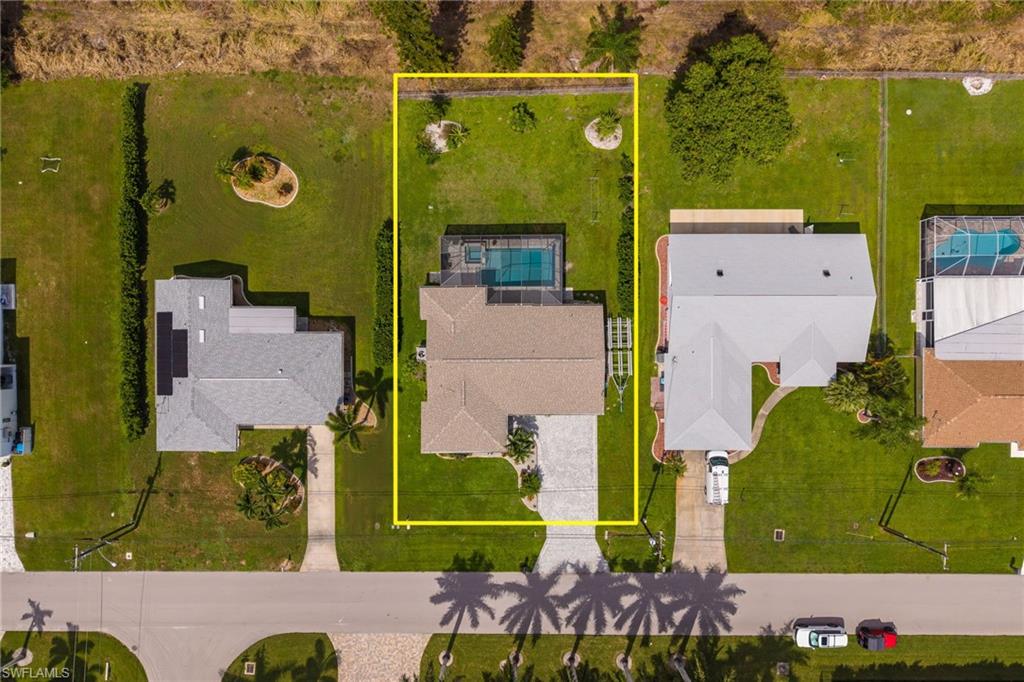 Aerial perspective showcasing a property with a swimming pool, paved driveway, and surrounding green lawn