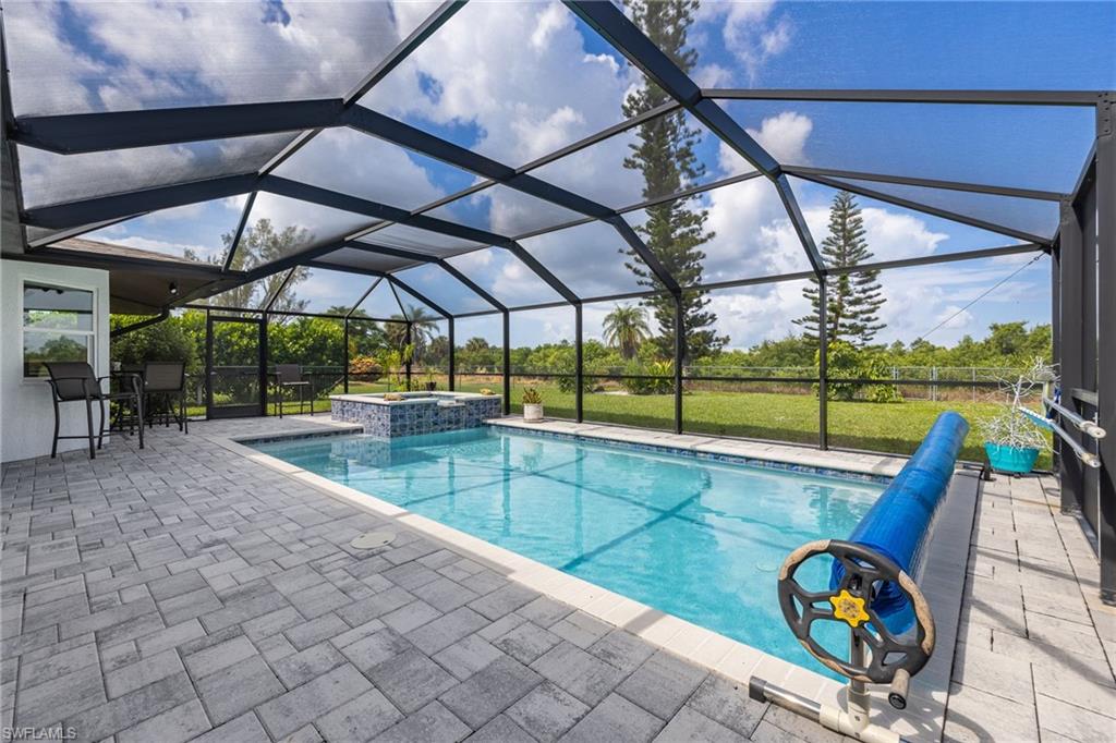 Screened enclosure featuring a swimming pool, integrated spa with tile detailing, and a spacious paver deck