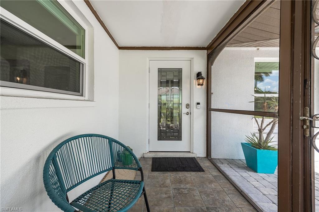 Covered front entry featuring a white door with decorative glass, an exterior wall sconce, and a tiled floor