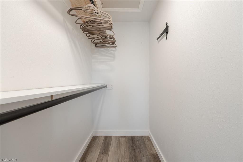 Walk-in closet featuring a built-in shelf and hanging rod, complemented by wood-finish flooring