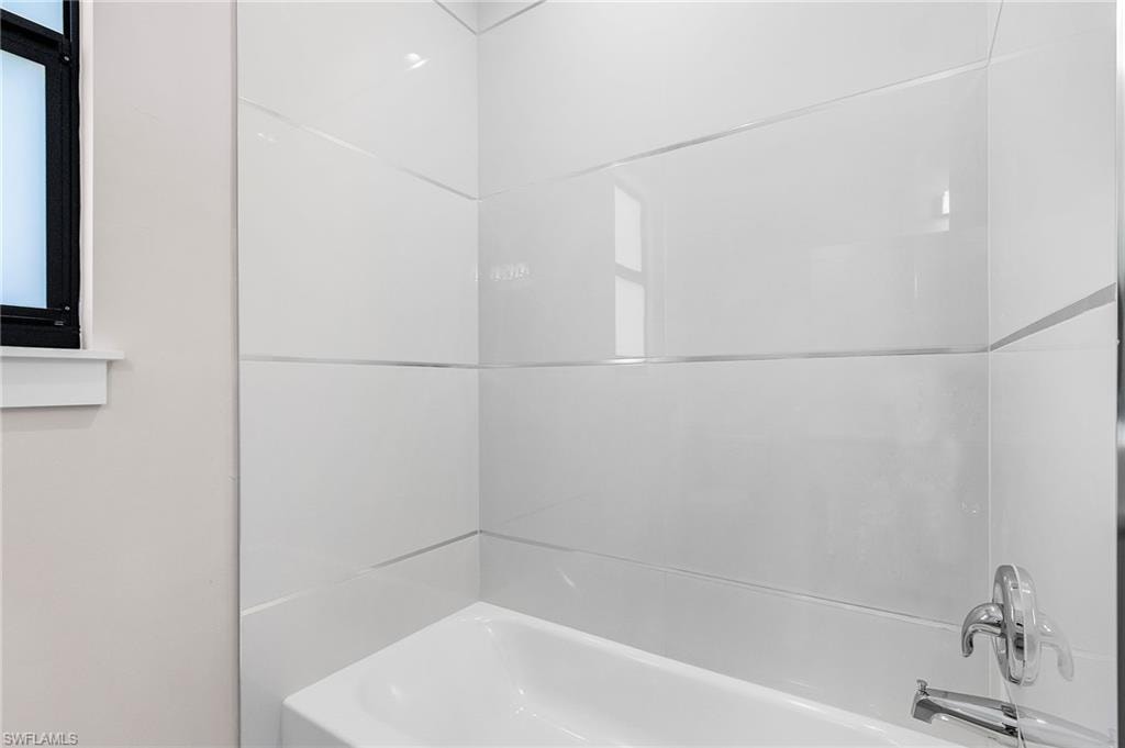Bathtub with a chrome fixture, white tile surround, and a black-framed window