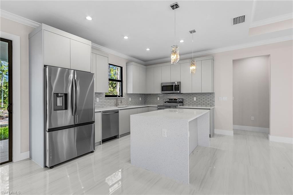 Modern kitchen featuring a waterfall island with a light-toned countertop, stainless steel appliances, light gray cabinetry, and a tile backsplash