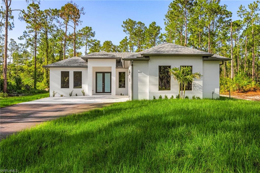 Contemporary white stucco exterior with dark-framed windows, a covered entry, and a double-door entrance, complemented by a concrete drive and natural landscaping