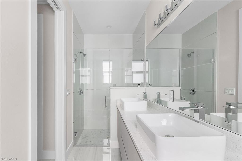 Dual vessel sinks with chrome faucets, a full-width mirror, and a glass-enclosed shower with a rain showerhead