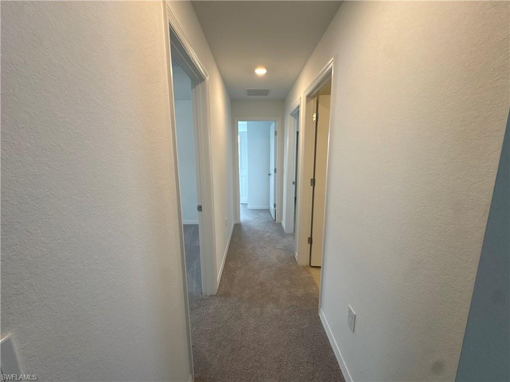 Carpeted hallway with white painted walls and recessed lighting