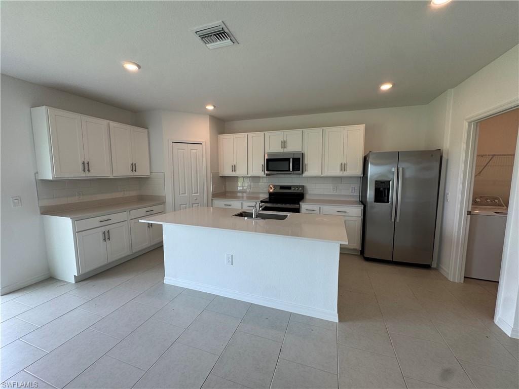 Kitchen featuring an island with an undermount sink, white cabinetry, light-toned countertops, and stainless steel appliances