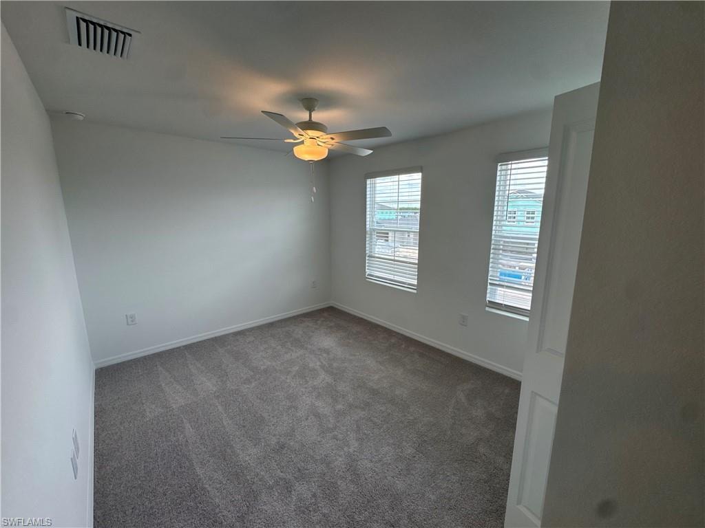 Neutral wall finishes, textured carpeting, two windows with blinds, a ceiling fan with integrated lighting, and a white paneled door