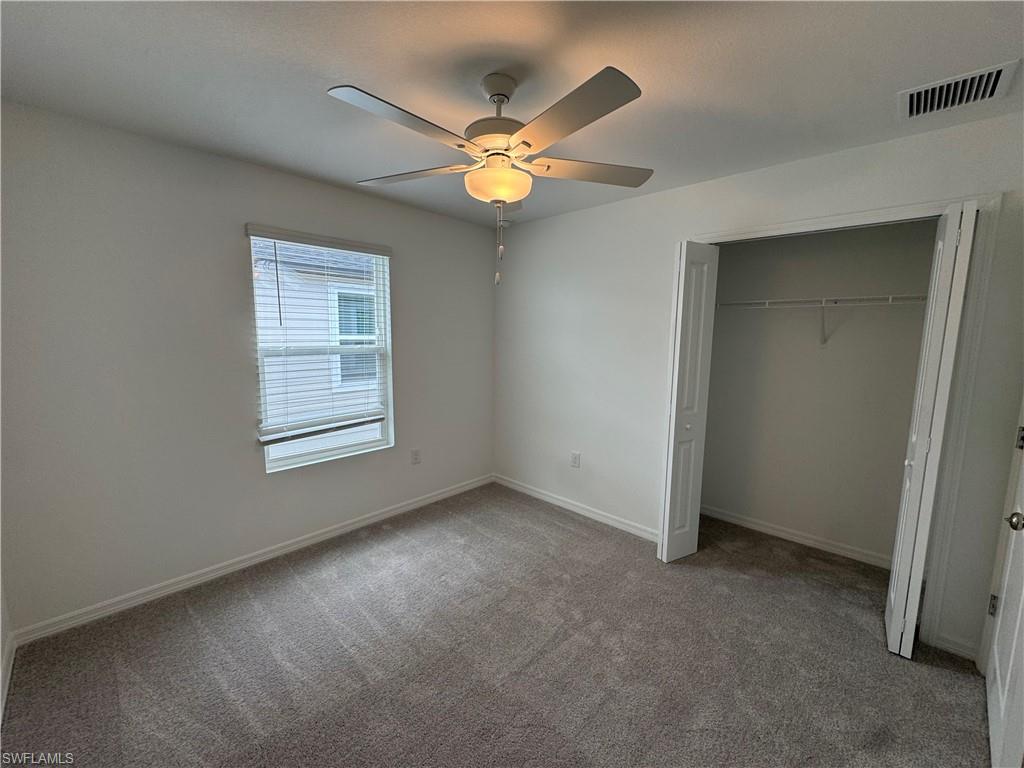 Neutral wall color, gray carpeting, a window with blinds, a ceiling fan with light, and a bi-fold door closet