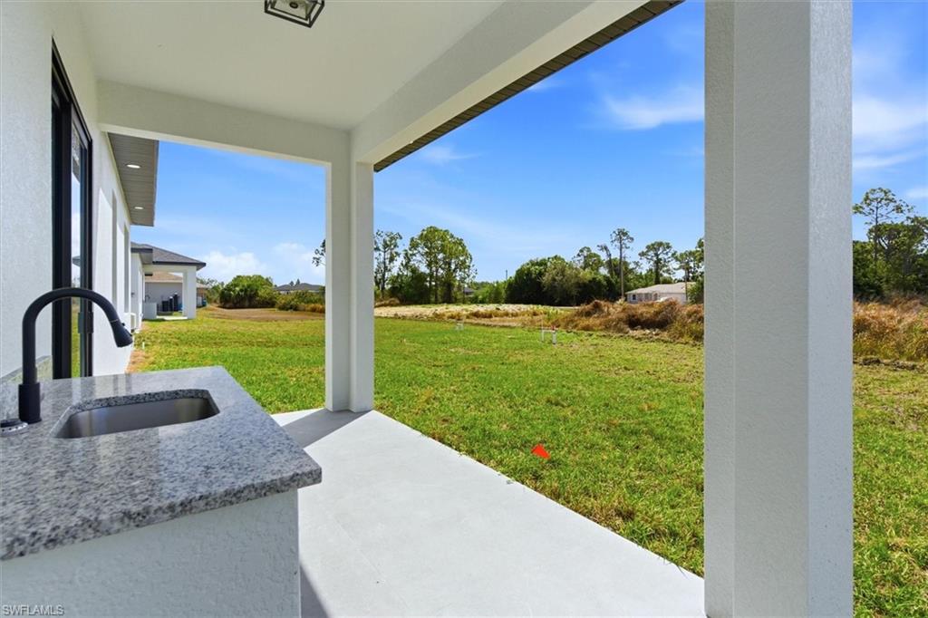 Covered outdoor patio with a built-in counter featuring a stainless steel sink and matte black faucet, set against a spacious green area