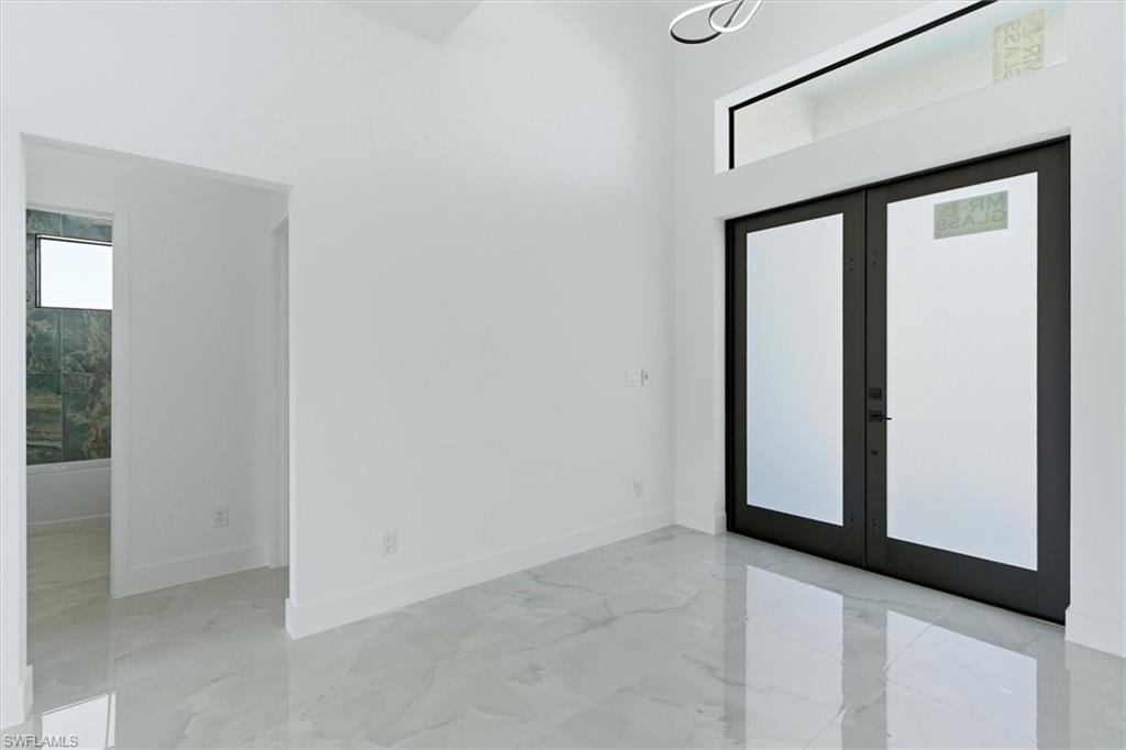 Vaulted ceiling, transom window, contemporary chandelier, double entry doors, and large format floor tile