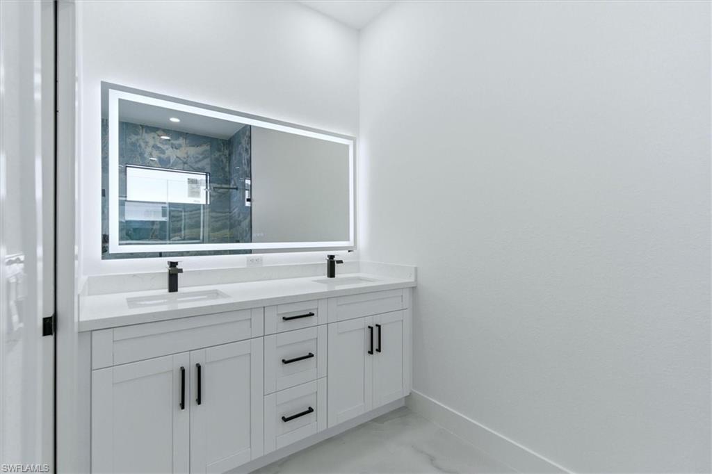Dual vanity with white cabinetry and matte black hardware, integrated sinks, white countertops, and an illuminated mirror