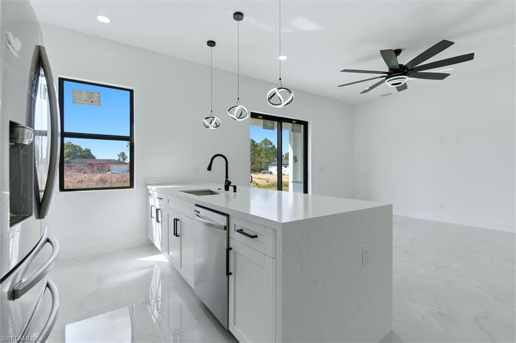 Spacious kitchen island with a white countertop and integrated sink, modern pendant lighting, white cabinetry with black hardware, and an expansive ceiling fan