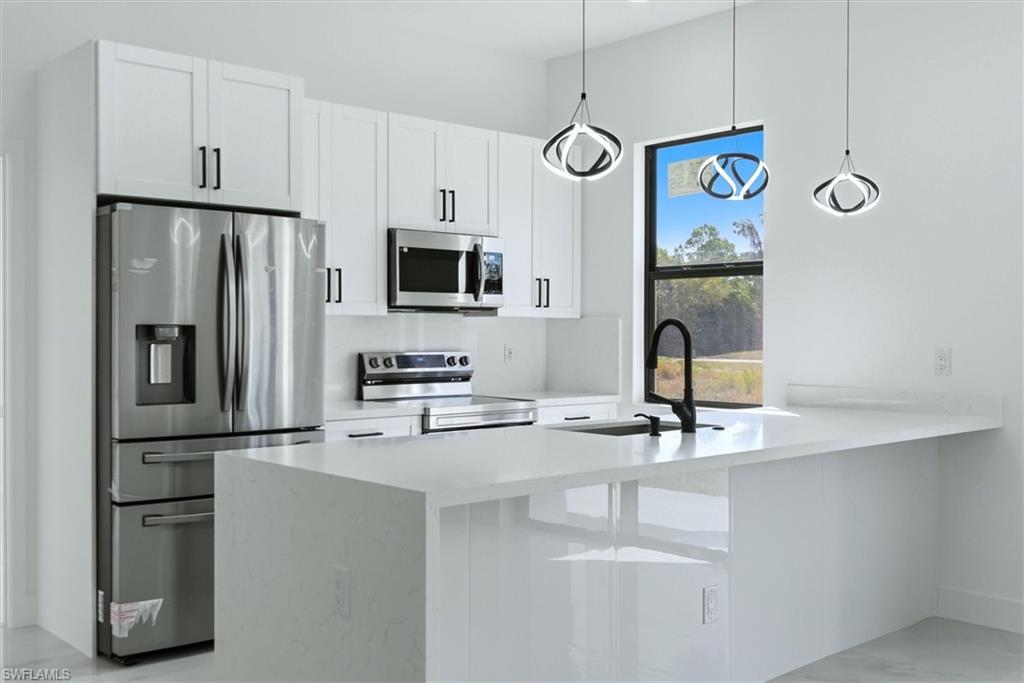 Modern kitchen featuring white cabinetry, stainless steel appliances, a white island with a built-in sink, a matte black faucet, and contemporary pendant lighting